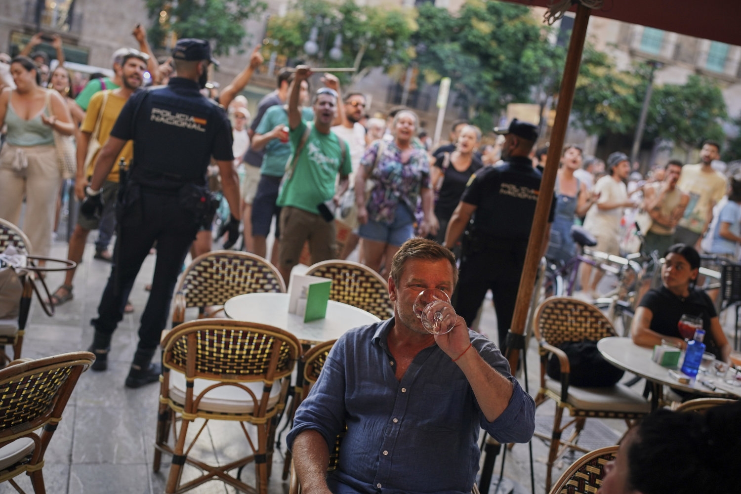 Turister sitter på en restaurant på Mallorca mens de fastboende spanjolene demonstrerer mot overturisme. 